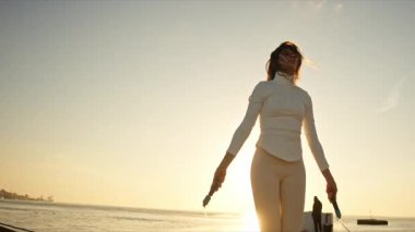 Güneş doğarken iskelede atlama halatıyla antrenman yapan kadın sporcu.