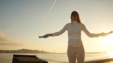 Enerjik kadın gün doğumunda nehrin kenarında atlama ipiyle egzersiz yapmaktan hoşlanıyor.