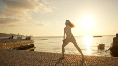 Gün batımında nehir kenarında esneme egzersizleri yapan bir kadın.