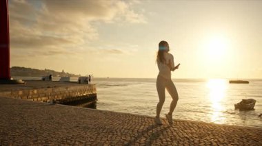 Gün batımında Lizbon 'da nehir kıyısında koşan enerjik genç bir kadın.