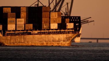 21 Mayıs 2025, Lisbon. Portekiz - Bir konteyner gemisinin yanında gezinen feribot altın rengi bir günbatımında