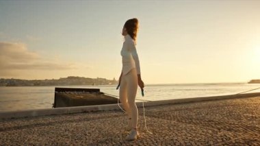 Gün batımında nehir kenarında egzersiz yapan, ip atlayan genç bir kadın.