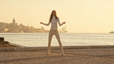 Gün batımında bir iskelede dans eden kadın, altın saatin tadını çıkarıyor.