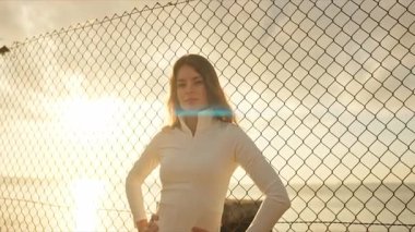 Genç sporcu tel örgülere karşı poz veriyor ve arkasında güneş doğuyor.