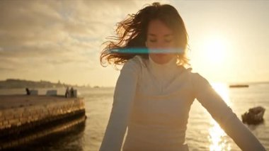 Gün batımında deniz kenarında dans eden genç bir kadın.