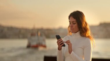 Günbatımında Bosphorus Boğazı yakınlarında akıllı telefonunu kullanan genç bir kadın, İstanbul.