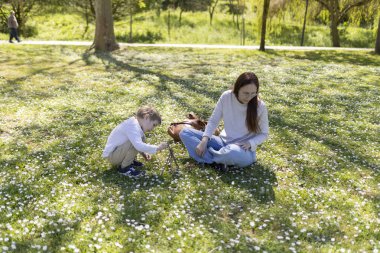 Genç anne ve oğul, papatyalarla dolu bir parkta güneşli bir bahar gününde dallarla küçük yapılar inşa ederek kaliteli zaman geçiriyorlar.
