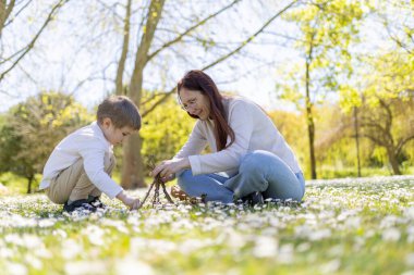Anne ve oğlu güneşli bir parkta bir değnek yapı inşa ediyorlar.