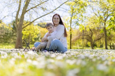 Anne ve oğul, yemyeşil ve ılık gün ışığıyla çevrili güzel papatya tarlasında birlikte güzel vakit geçiriyorlar.
