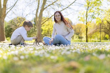 Anne ve oğlu parkta güneşli bir günün tadını çıkarıyorlar. Papatya tarlasında çubuklarla küçük bir çadır kuruyorlar.