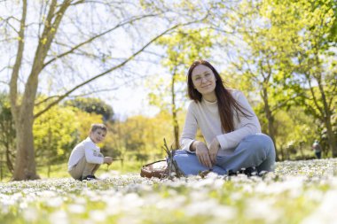 Anne ve oğlu güneşli bir bahar gününde papatya tarlasında dinleniyorlar.