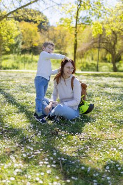 Mutlu anne ve çocuk papatyalarla çevrili bir parkta güneşli bir bahar gününün tadını çıkarıyor.