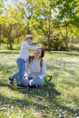 Mutlu anne ve oğul papatya dolu bir parkta güneşli bir bahar gününün tadını çıkarıyor.