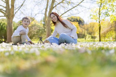 Anne ve oğlu baharda beyaz çiçeklerle dolu bir arazide birlikte küçük bir sopa evi inşa ediyorlar.