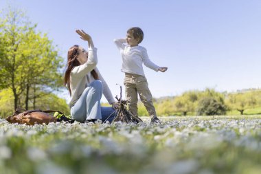Anne ve oğlu çiçek tarlasında eğleniyor güneşli bir günde kamp ateşi yakmaya hazırlanıyor.