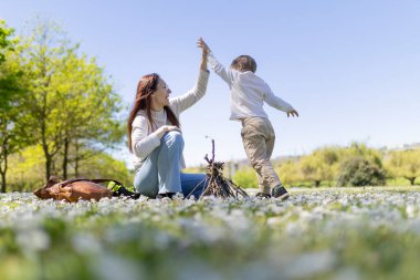 Anne ve oğlu çiçek tarlasında eğleniyor, güneşli bir günde küçük bir şenlik ateşi yakıyor.