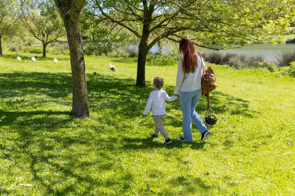 Anne ve çocuk güneşli, yeşil bir parkta huzurlu bir yürüyüş yapıyorlar.