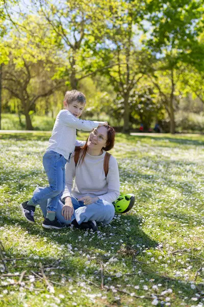 Mutlu anne ve oğul papatya dolu bir parkta güneşli bir bahar gününün tadını çıkarıyor.