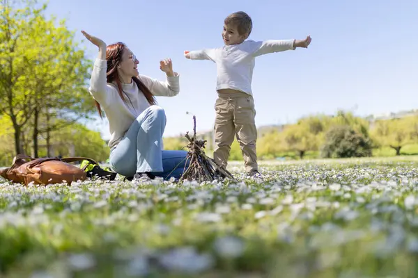 Anne ve oğul çiçek tarlasında oynuyorlar ve güneşli bir günde küçük bir şenlik ateşi yakıyorlar.