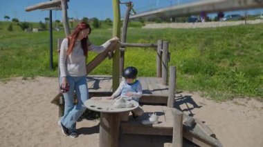 Anne, oğlunun çocuk parkında paten giymesine yardım ediyor.