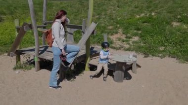 Paten tutan genç bir anne oğlunu parkta oynarken seyrediyor.