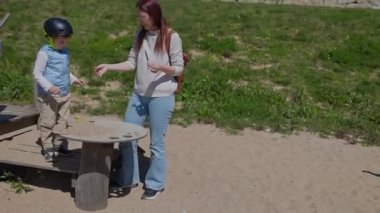 Kask takan genç bir çocuk annesiyle oyun masasında kumla oynuyor.