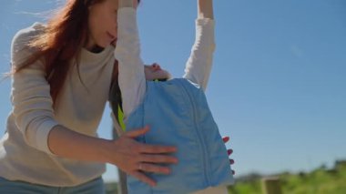 Anne, oğlunun oyun parkında oynarken kaskını ve yeleğini giyiyor.