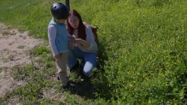 Anne oğluna doğayı öğretiyor, ona küçük sarı çiçekleri gösteriyor.
