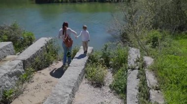 Anne ve oğlu dikkatle inen taş basamaklar bir nehir kıyısına yakın.