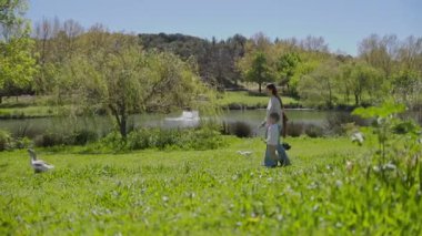 Anne ve oğlu ördeklerle çevrili bir gölün kenarındaki gölün keyfini çıkarıyorlar.