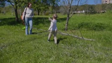 Neşeli çocuk, güneşli bir günde ebeveynleri onu izlerken yeşil bir parktaki büyük bir dalla etkileşime girer.