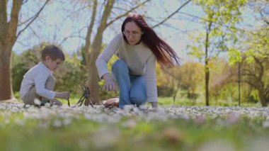 Anne ve oğul, serin bir parkta, çiçek açan çimen ve ağaçların arasında çubuk toplayarak güzel vakit geçiriyorlar.