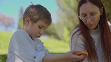 Anne ve oğlu güneşli bir parkta piknik yaparken hamburger yiyorlar.