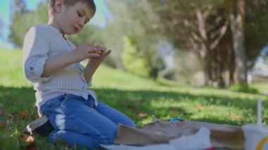 Çocuk, annesi yakınlardayken parkta atıştırmanın tadını çıkarıyor.