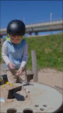 Kask takan, oyun masasında çiçeklerle kumdan kale süsleyen genç bir çocuk.