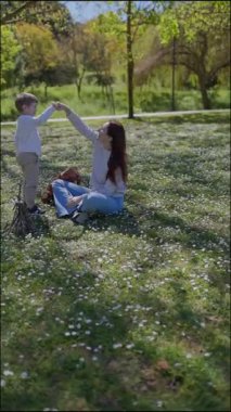 Anne ve oğul birlikte güzel vakit geçiriyorlar. Beyaz çiçeklerle dolu bir parkta oynuyorlar.