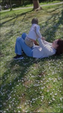 Mutlu anne oğluyla küçük beyaz çiçeklerle dolu bir parkta kaliteli vakit geçirmekten hoşlanıyor.