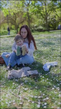 Anne, güzel bir günde parkta yürümeye yeni başlayan çocuğuna ayakkabı giydirmeye yardım eder.