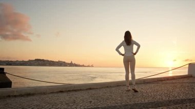 Nehir kenarında gün doğumunda spor yapan kadın bacak egzersizi yapıyor.