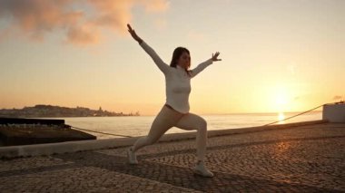 Yoga eğitmeni gün doğumunda nehir kenarında poz veriyor.