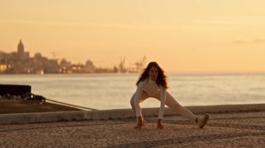 Yoga yapan esnek sporcu kadın şafak vakti asfaltlı bir yüzeyde bir su kütlesinin yanında poz veriyor.
