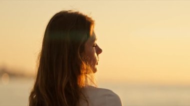 Kulaklıklı sakin kadın deniz kenarında huzurlu bir gün batımının tadını çıkarıyor.