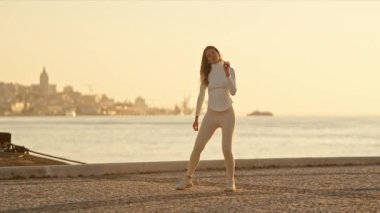 Gün batımında deniz kenarında zarif bir şekilde dans eden genç kadın, yeteneğini ve hareket tutkusunu sergiliyor.