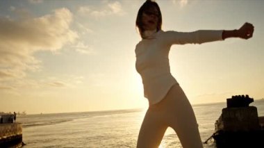 Gün batımında iskelede dans eden kadın, altın saatin tadını çıkarıyor.