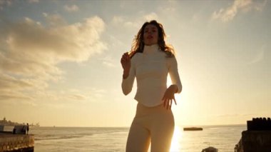 Gün batımında deniz kenarında dans eden genç bir kadın.