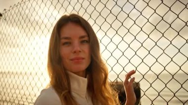 Bir kadın, okyanusa bakan, gün batımının sıcak ışığıyla aydınlatılan zincirli bir çitin yanında dururken huzurlu bir an. Huzurlu ve düşünceli bir ortam.