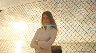 Gün batımında bir plajda çapraz kollarla poz veren genç bir bayan sporcu.