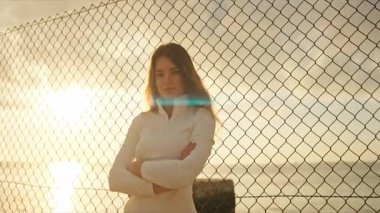 Gün batımında deniz kenarında çapraz kollarla poz veren genç bayan sporcu.