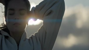 Saçlarını başının arkasında tutan genç bir kadın, günbatımının tadını çıkarıyor.