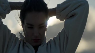 Gün batımında saçlarını tutan genç bir kadın.